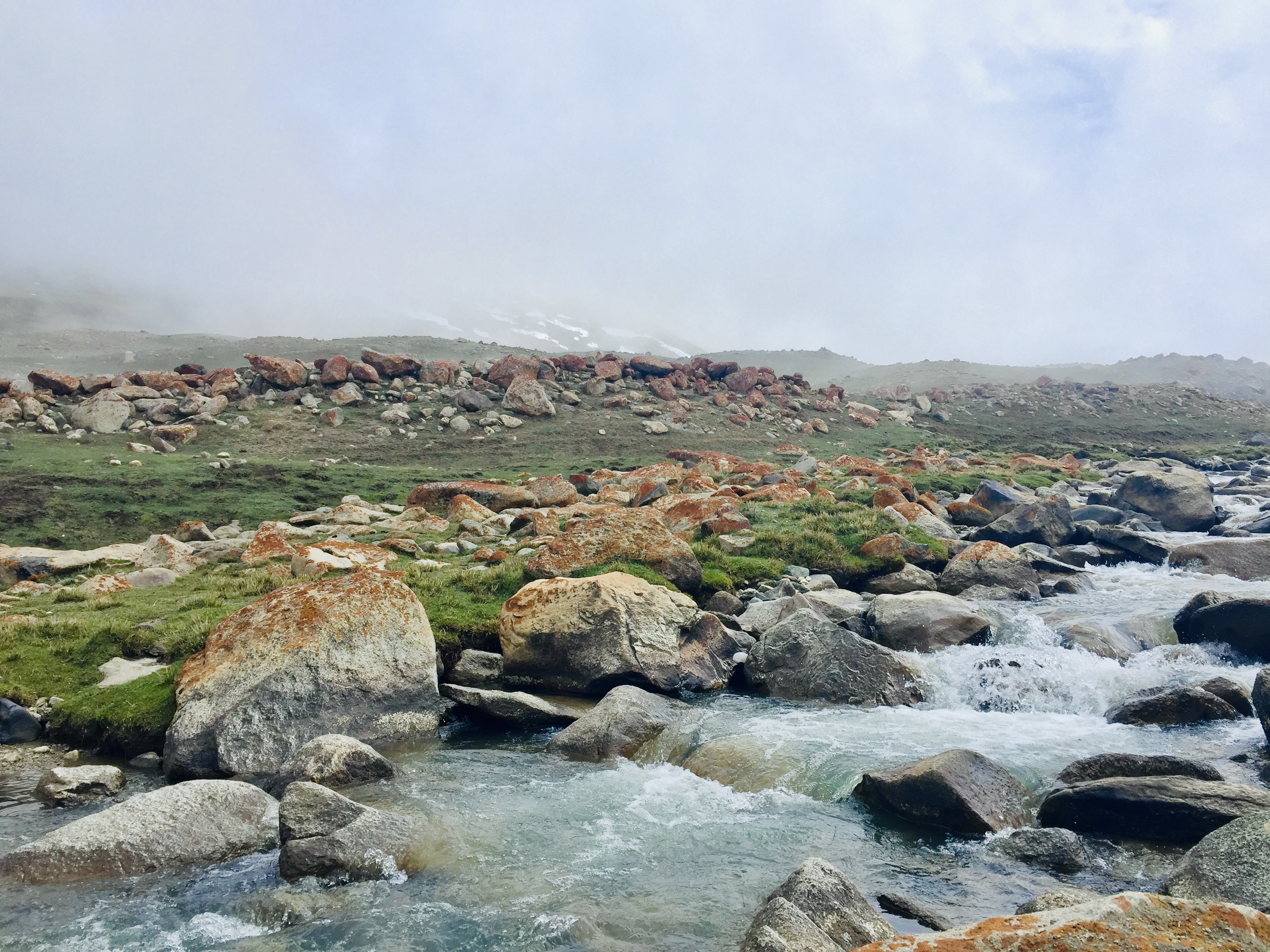 A stream in Ladakh, gurgling through rocks, mist and clouds